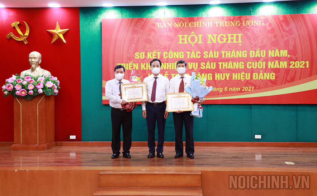 Đồng chí Lại Xuân Lâm, Phó Bí thư Đảng ủy Khối các cơ quan Trung ương tặng hoa chúc mừng 2 đồng chí nhận Huy hiệu 30 năm tuổi Đảng